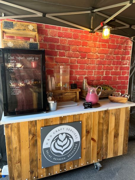 Wooden stall with a glass display, teapot, and a brick wall background.
