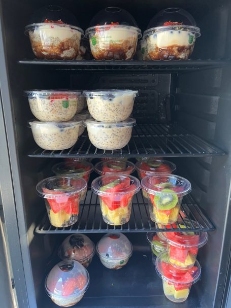 Assorted desserts in plastic cups, including fruit and rice pudding, stored in a fridge.