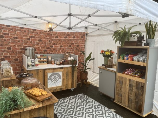 A rustic food stall with wooden decor, plants, and a variety of baked goods displayed.