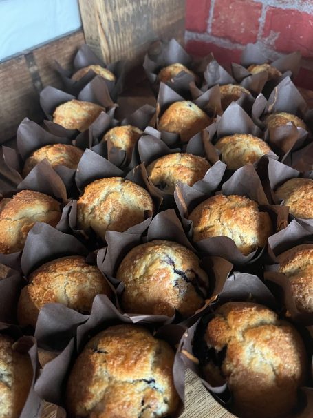 Freshly baked muffins in brown paper liners, arranged in a wooden box.