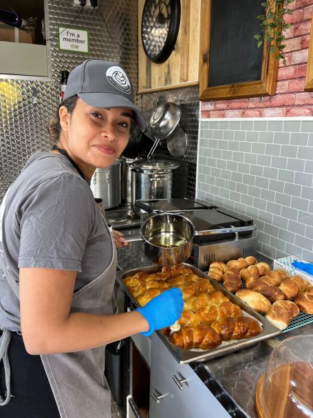 A woman prepares food in a kitchen, wearing a grey cap and blue gloves.