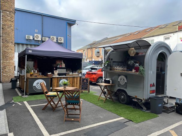 Food truck and vendor tent set up with small tables in a parking lot.