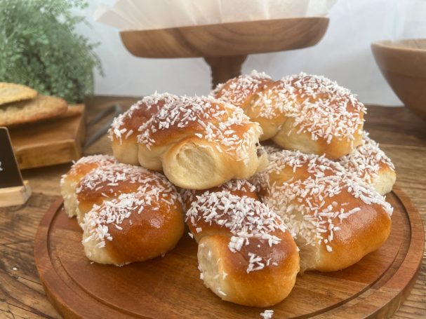 Freshly baked sweet rolls topped with white sprinkles, served on a wooden platter.