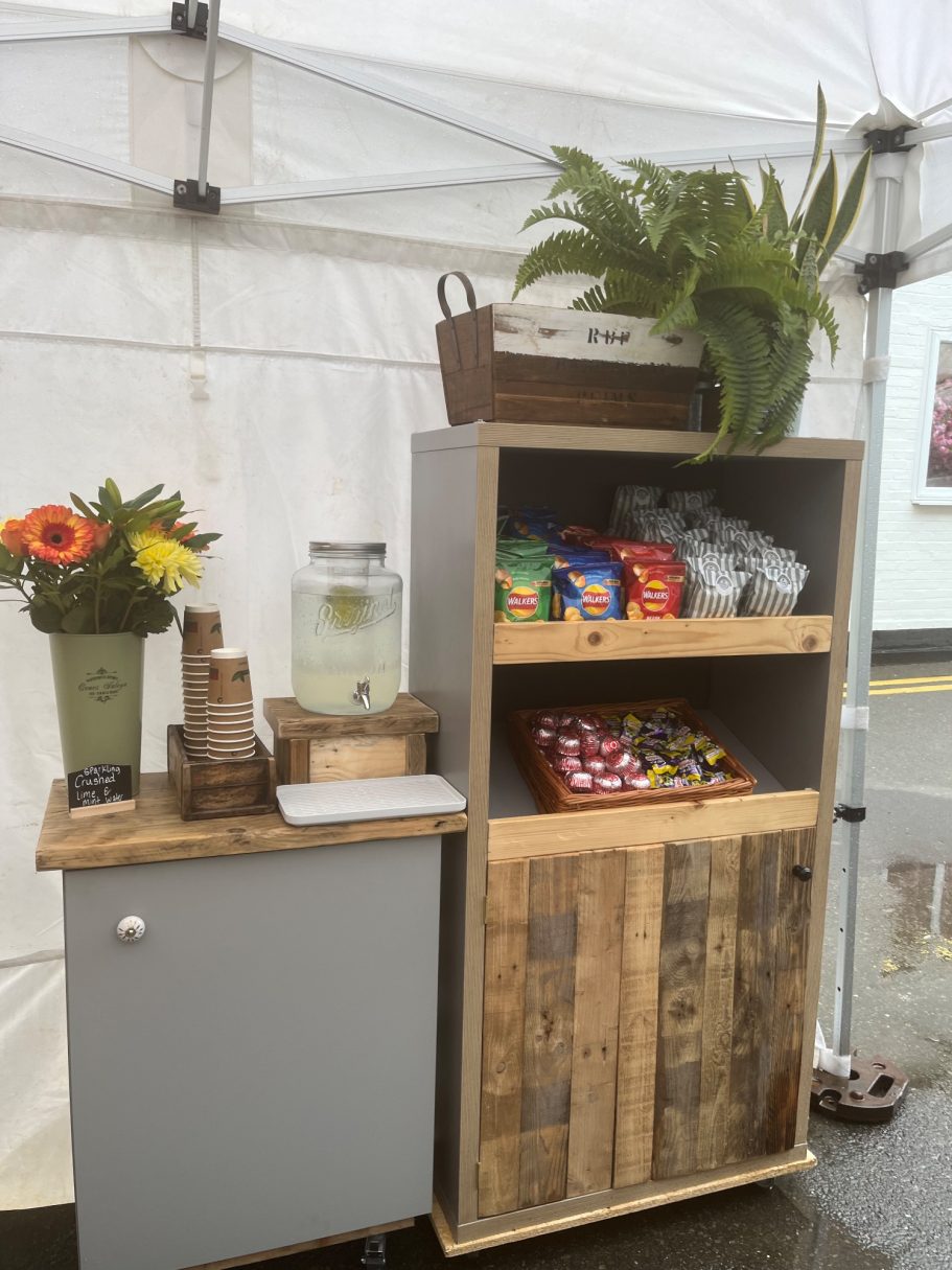A wooden stall displaying snacks and a decorative flower arrangement.