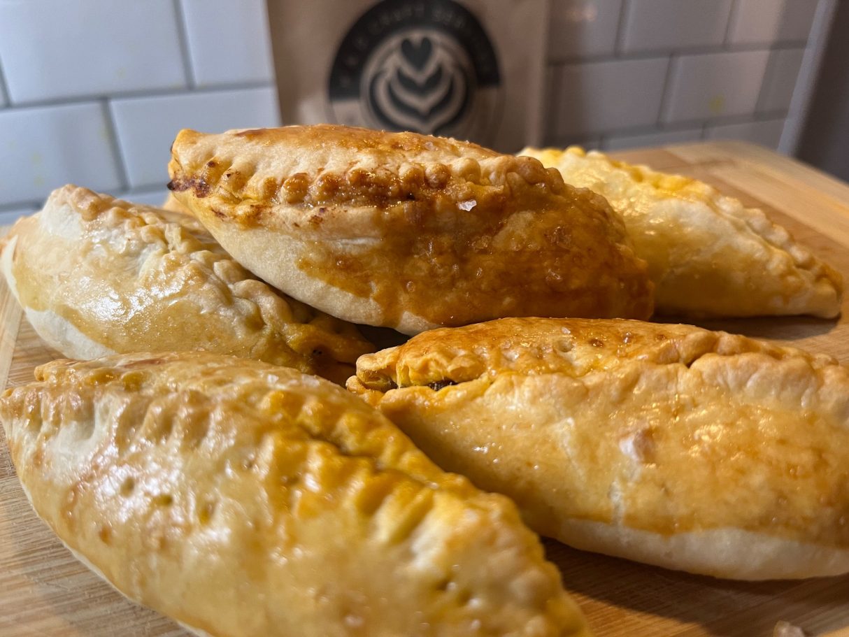 Golden-brown pastres with crimped edges, filled and stacked on a wooden surface.