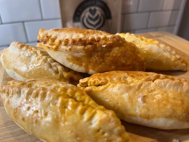 Golden-brown pastres with crimped edges, filled and stacked on a wooden surface.