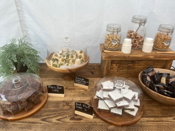 A selection of desserts and snacks displayed under glass cloches on a wooden table.
