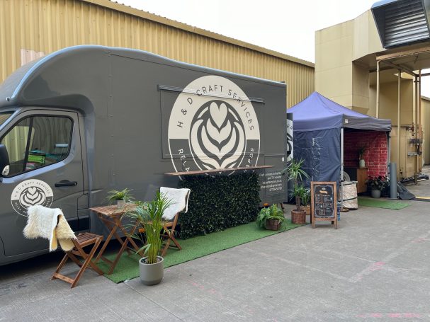 Our Beautiful food truck with our logo, surrounded by small plants and outdoor furniture on-set at the studio.