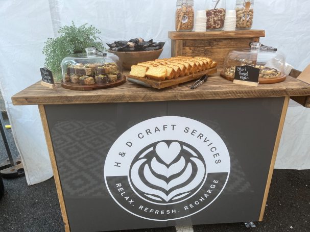 Wooden display table with assorted sweets and treats, featuring jars and a logo.