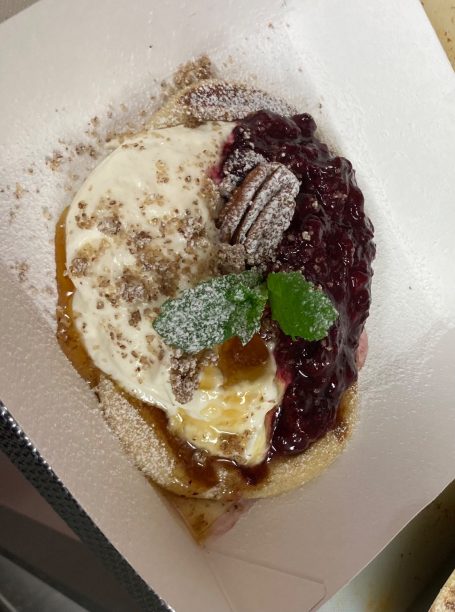 A dessert with cream, berry sauce, and mint garnish on a plate.