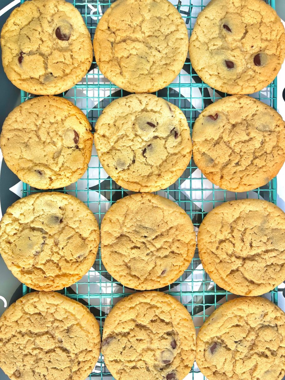 Twelve freshly baked chocolate chip cookies on a cooling rack.