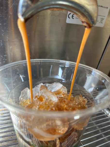 Brewed coffee pouring over ice in a glass container.