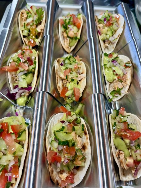 Several tacos filled with fresh vegetables, tomatoes, and herbs arranged neatly in a tray.