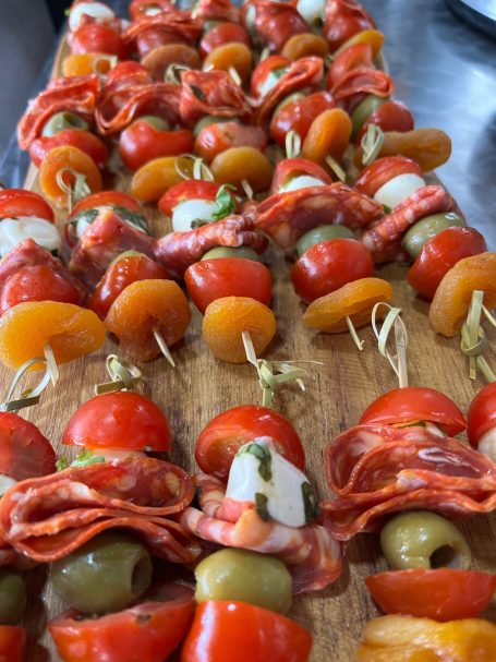 Skewers with cherry tomatoes, olives, salami, and dried apricots on a wooden board.